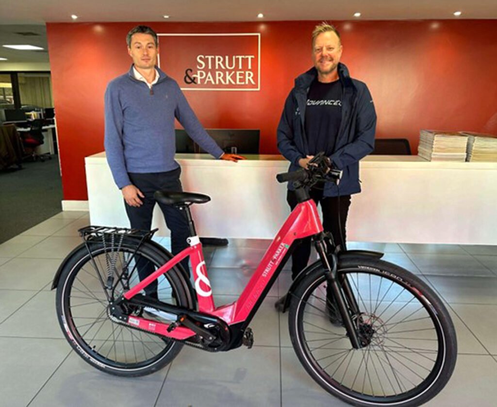 Two white men standing in front of reception desk in estate agent office. In the foreground is a smart pink ebike