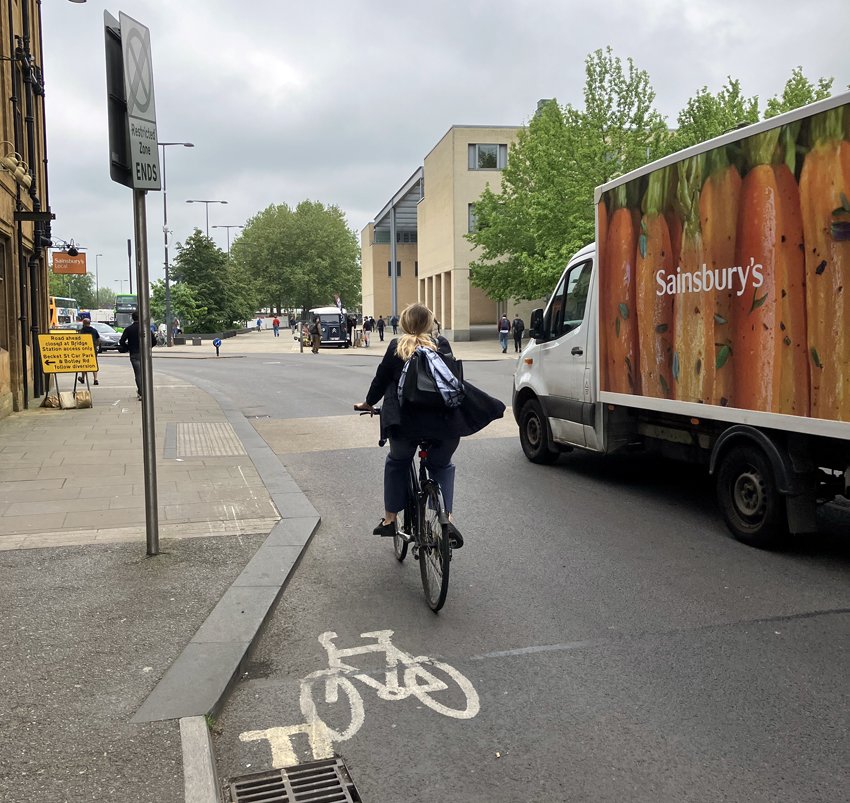 Cyclist on the road having to veer into traffic as painted cycle lane disappears. Large Sainsbury's truck to right of cyclist