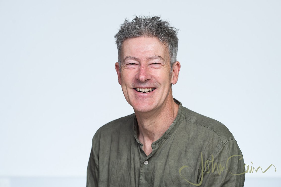 Portrait of Ian Loader. White man with short spiky grey hair in open-necked khaki shirt