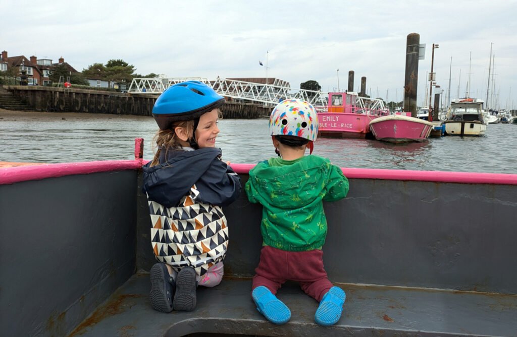 Back view of two small children kneeling in front of boat looking out at harbour